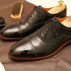 Paire de richelieus noirs brillants, prêts pour un glacage chaussure parfait. Pot de cirage et brosse à proximité.