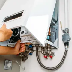 Tecnico che regola la pressione del gas dello scaldabagno, mostrando i collegamenti idraulici e il pannello di controllo.
