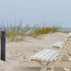 Białe ławki na drewnianej promenadzie w Dziwnowie, z widokiem na piaszczyste wydmy i morze.