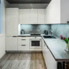 Nowoczesna kuchnia z białymi frontami i betonowym backsplash. Wygodny układ i funkcjonalne rozwiązania, idealne do planowania remont kuchni koszt.