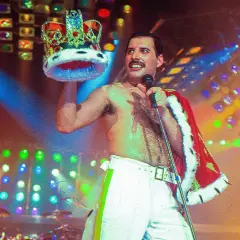 Freddie Mercury, w koronie i z mikrofonem, na scenie pełnej świateł. Pamięć o nim żyje, choć zmarł Freddie Mercury.