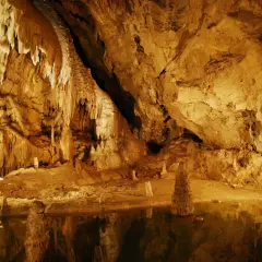 Wnętrze jaskini z naciekami i stalagmitami, odbijającymi się w wodzie. Tajemnicze piękno Tatr Bielskich.