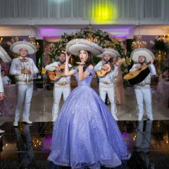 Mariachi grają przyśpiewki weselne, a młoda kobieta w fioletowej sukni posyła całusy.
