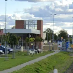 Nowoczesna stacja kolejowa z budynkiem, peronem, ławkami i parkingiem.