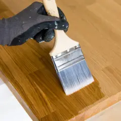 Maintenant, peut on vernir après huile de lin ? Un pinceau applique une couche transparente sur un plateau en bois.
