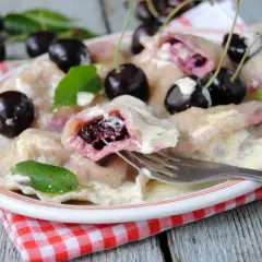 Pyszne pierogi z czereśniami, polane śmietaną, ozdobione świeżymi owocami i listkami mięty. Idealne na letni deser.