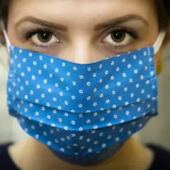 Oczy młodej kobiety patrzą zza niebieskiej maseczki w białe kwiatuszki. W czasach covidu, nawet niska temperatura nie zwalnia od noszenia maseczki.