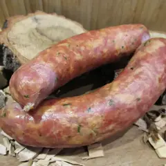 Dwie świeże kiełbasy, idealnie doprawione majerankiem, leżą na drewnianych plastrach.