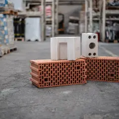 Cegły ceramiczne i białe pustaki na szarym tle, w tle magazyn budowlany.