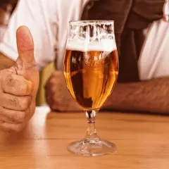 Kciuk w górę obok kieliszka ze złotym бланш пиво. Idealny wybór na relaks.