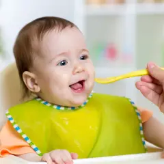 Uśmiechnięte dziecko w śliniaczku dostaje łyżeczkę jedzenia dla niemowlaka.