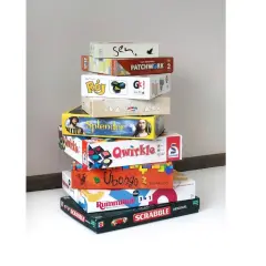 Stos pudeł z grami planszowymi, idealnymi na rodzinne wieczory. Wśród nich "Splendor", "Qwirkle", "Ubongo" i "Scrabble" – świetna gra dla seniorów.