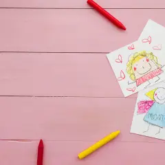 Dziecięce rysunki i kredki na różowym tle. Może to być ilustracja do sprawy o pozew o alimenty na dwoje dzieci.