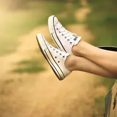 Nogi w białych trampkach wystawione z okna samochodu na tle rozmytego krajobrazu.