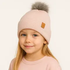 Uśmiechnięta dziewczynka w pudrowym komplecie z pomponem na czapce. Idealny komin dla dziecka na zimowe zabawy.