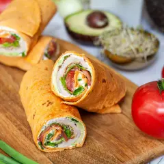 Pyszna tortilla z szynką, świeżymi warzywami i kremowym serkiem, ułożona na desce z dodatkami.