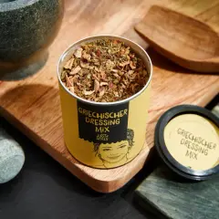 Dose mit Gewürzmischung für original griechischer salat dressing, daneben Mörser und Holzschale.