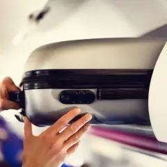 Ręce wkładają srebrną walizkę do schowka nad głową w samolocie. Czas na podróż z Malta Air!