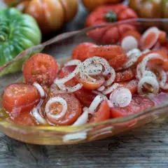 En skål med skivad tigerella tomat och lök, kryddad med peppar. Bakom syns fler tomater i olika färger.