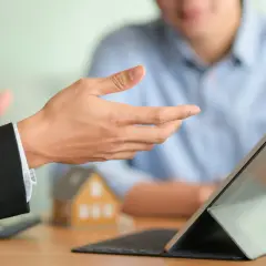Doradca omawia, jak wynająć mieszkanie, wskazując na tablet. W tle model domu.