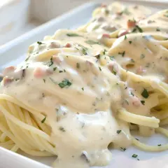 Cremige Spaghetti Carbonara mit Speckwürfeln und Petersilie, serviert auf einem weißen Teller.