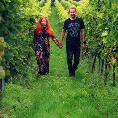 Para spaceruje po winnicy na Dolnym Śląsku, trzymając się za ręce. Wokół bujna zieleń i dojrzewające winogrona.