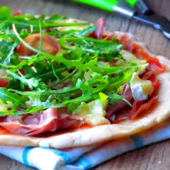Pyszna pizza parma z rukolą i serem na drewnianym blacie.