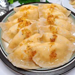 Talerz pełen pysznych pierogów ruskich, polanych tłuszczem i posypanych skwarkami. Idealne, by pokazać, jak zrobić pierogi ruskie.