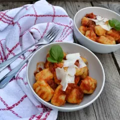 Dwa talerze pysznych gnocchi z sosem pomidorowym, posypane parmezanem i udekorowane bazylią, gotowe do podania.