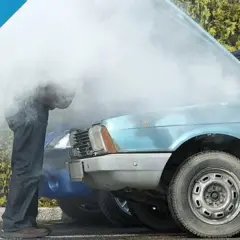 Uomo guarda motore fumante di un'auto blu, probabile perdita liquido refrigerante.