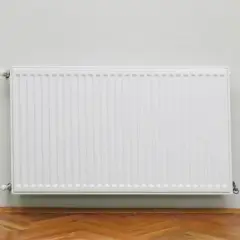 Radiatore bianco moderno su parete chiara, con parquet. Utile per calcolare quanti elementi termosifoni per mq.
