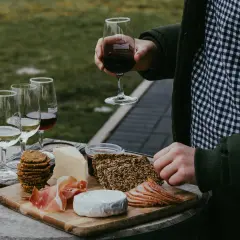 Un plateau de fromages, charcuteries et biscuits accompagne un verre de vin rouge. Une dégustation parfaite de vin et volailles en plein air.