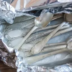 Stos srebrnych łyżek i widelców owiniętych w folię aluminiową.