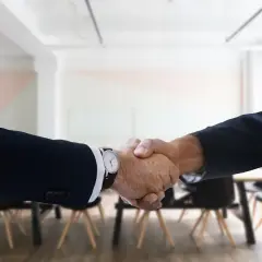Two men in suits shake hands, a gesture of how to be professional with coworkers.
