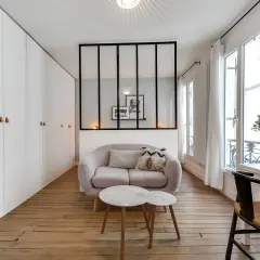 Ein moderner Raumteiler mit schwarzen Metallstreben trennt den Wohnbereich mit einem Sofa und Couchtisch vom Rest des Zimmers.