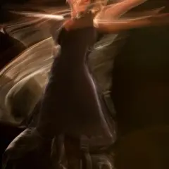 Una figura etérea en un vestido oscuro se mueve con gracia, sus brazos extendidos crean estelas de luz. Es como soñar con bailar, un instante capturado en movimiento.