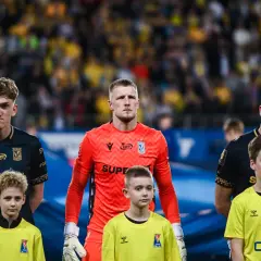Bramkarz Lecha Poznań w pomarańczowej koszulce stoi obok młodych zawodników.