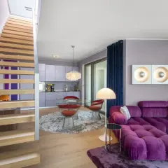 Ein Wohnbereich im 70er jahre einrichtungsstil mit lila Sofa, runden roten Stühlen und einer Holztreppe.
