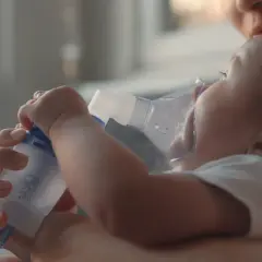 Mama pomaga maluszkowi z mokrym kaszlem u niemowlaka, stosując inhalator.