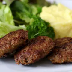 Drei goldbraune Fleischpflanzerl liegen auf einem Teller neben Kartoffelpüree und Salat. Ein leckeres Fleischpflanzerl Rezept zum Nachkochen.