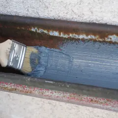Hand streicht mit Pinsel graue Farbe auf rostige Dachrinne zum dachrinne abdichten.