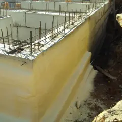 Zastosowano izolację pionową fundamentów. Widać zbrojenie i betonowe ściany fundamentowe, a obok wykop z ziemią.