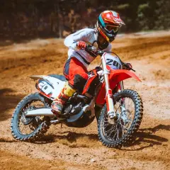 Motociclista in azione su pista sterrata, con la sua moto personalizzata da adesivi sportivi.