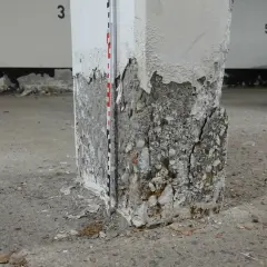 Betonsäule mit starker Abplatzung und Rissen, Messlatte zur Schadensdokumentation. Die STB Decke ist hier stark beschädigt.