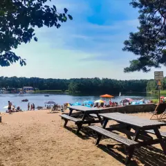 Słoneczny dzień nad jeziorem Średnim Turawa. Ludzie odpoczywają na plaży, kąpią się i pływają.