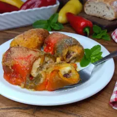 Involtini di peperoni ripieni, dorati e succulenti, serviti su un piatto bianco con menta fresca.