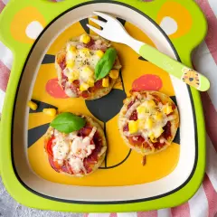 Schneller Pizzatag mit Quark: Kleine Mini-Pizzen mit Mais und Käse auf einem lustigen Teller, bereit zum Genießen.