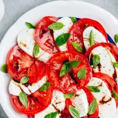 Sałatka caprese: plastry soczystego pomidora z mozzarellą, skropione balsamico i udekorowane listkami bazylii.