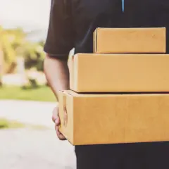 Kurier firmy kurierskiej FedEx niesie trzy paczki.