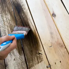 Mano che applica impregnante su assi di legno, recuperando un vecchio tavolo rovinato dalle intemperie.
